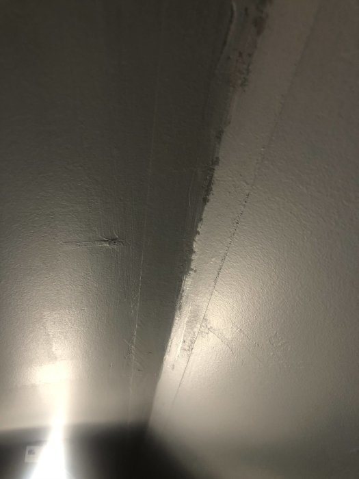 Gipsvägg med synliga pappremsor och bubblor efter spackling och målning.