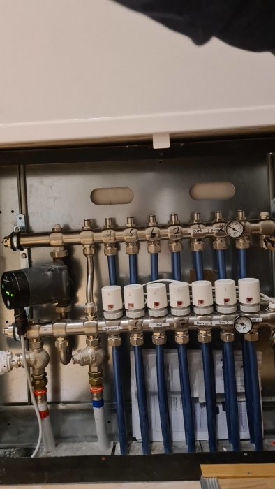 Värmesystems fördelare med numrerade ställdon och rör kopplade till värmeinstalltion.