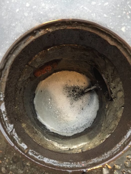 Brunn med småsten och bubblor av vatten, två rör synliga under husets garagenedfart.