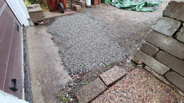 Nyanlagt dränerande material framför ett garage med befintligt grus och trottoarkant.