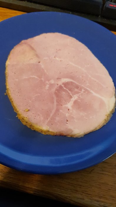 En skiva kokt skinka på en blå tallrik mot en bakgrund av ett trämöblerat skrivbord.