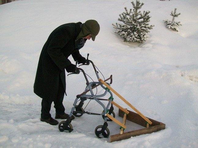 Person använder en hemmagjord snöröjningsutrustning med hjul på snöigt underlag.