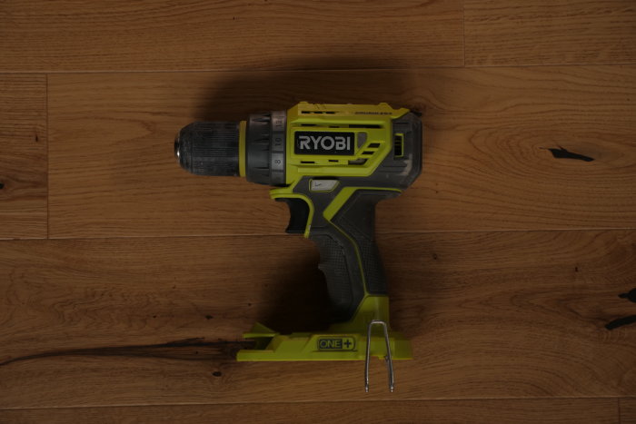 Ryobi skruvdragare i grönt och svart ligger på ett trägolv, modell R18DD7 med bälteskrok.