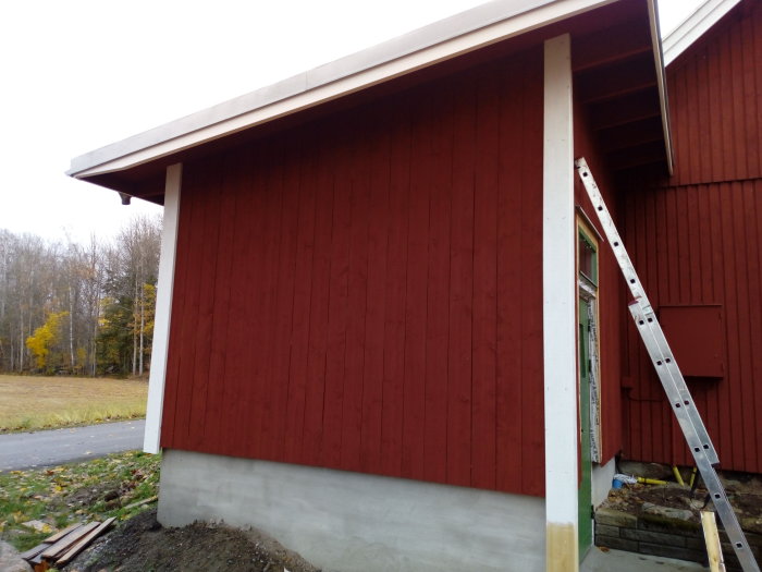 Nyuppsatta röda brädor på husknut med stege vid sidan och höstlöv på marken.