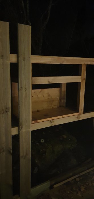 Träplank under konstruktion med en delvis inbyggd lockpanel, sedd i dunkel belysning.