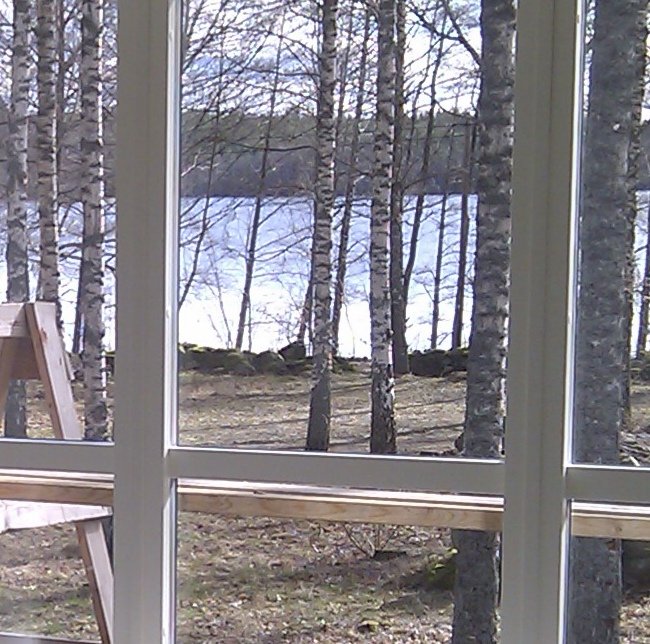 Utsikt över en sjö och björkar sett genom ett fönster från insidan av ett rum.