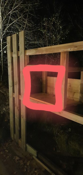 Ej färdigbyggd trägrind markerad med röd linje vid en mörk trädgård, behöver passande gångjärn.