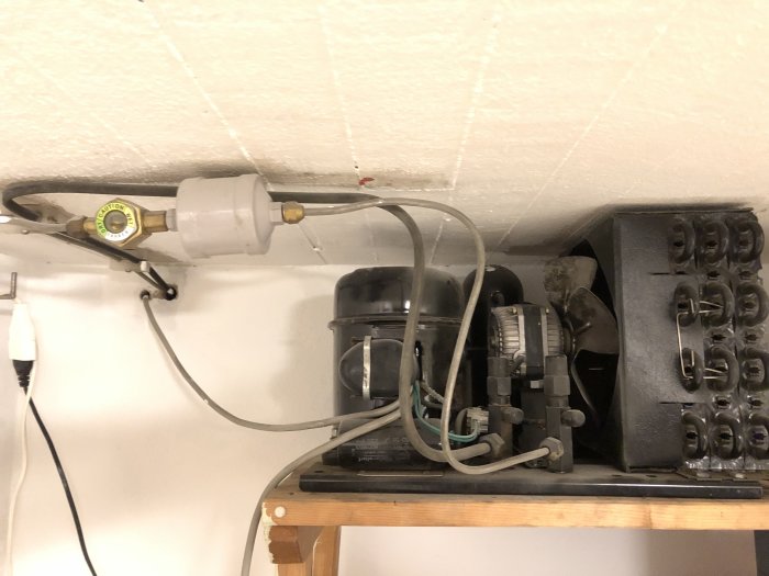 Äldre kylrumsutrustning utan köldmedium på trähylla, inklusive kompressor och anslutna rör.