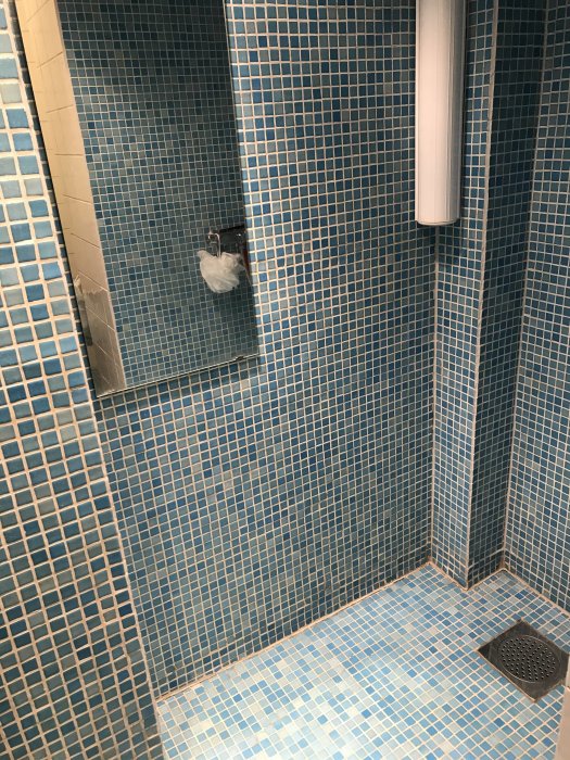Duschhörna med blå mosaik på väggar och golv samt installerad duschutrustning.