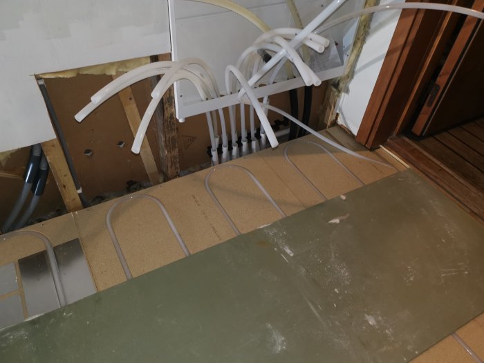 Installation av golvvärmeslangar på isolerat hallgolv och anslutning till fördelarskåp.