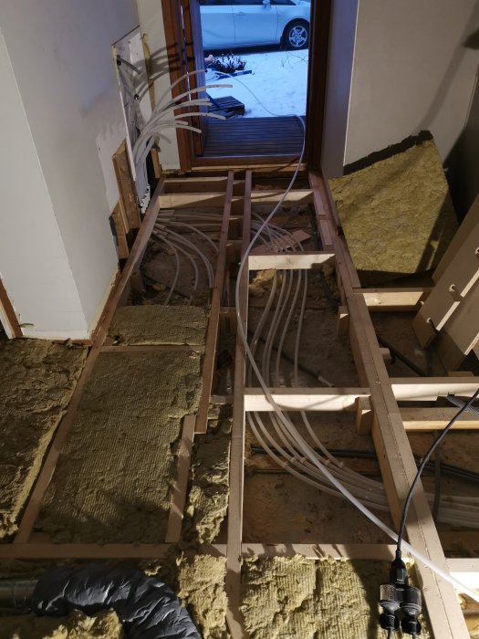 Installation av golvvärmeslangar mellan träbjälkar på ett isolerat hallgolv under konstruktion.