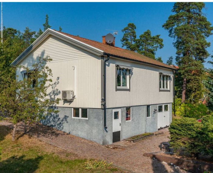 Tvåvåningshus från 40-talet med vit fasad och tegelrött tak omgivet av grönska, redo för renovering.