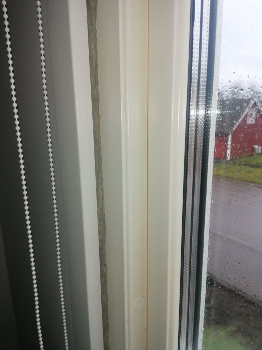 Isolering synlig mellan fönsterkarm och vägg i ett hem, med utsikt till regnigt fönster.