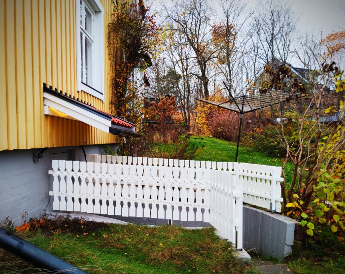 Nymålat vitt staket i allmogestil runt en liten avsats vid en gul husvägg.