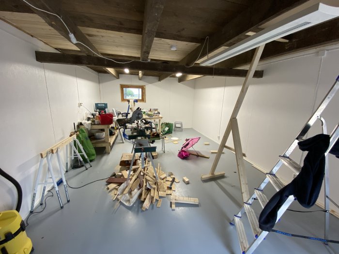 Översikt av ett pågående byggprojekt i ett rum med verktyg, byggmaterial och en stege.