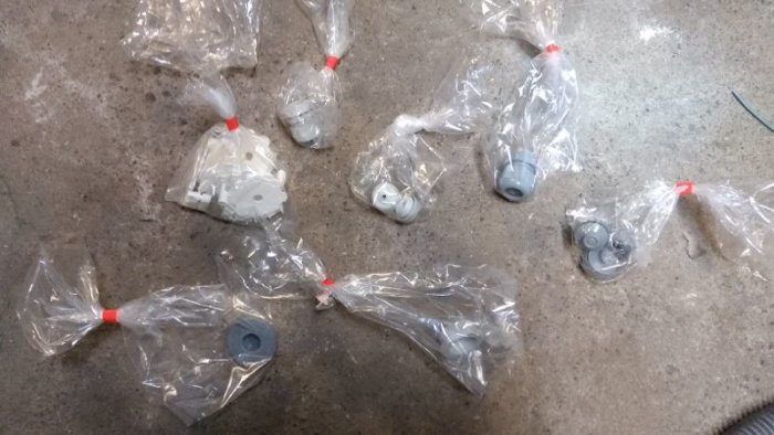 Flera små plastpåsar knutna med röda band innehållande olika små byggkomponenter.
