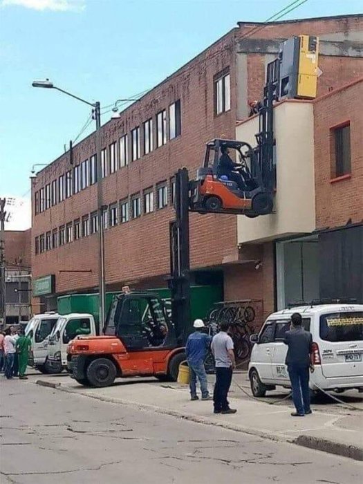 Gaffeltruck lyfter en annan truck på gata med tunt spännband.