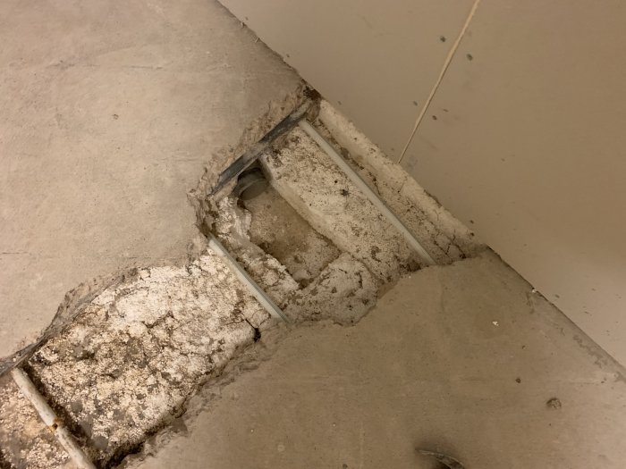 Öppning i betonggolv avslöjar underliggande rör och skadad slang vid byggprojekt.