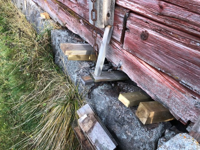 Gammal ladugårdsbyggnad med sjunken stengrund och tillfällig förstärkning med träblock under väggen.