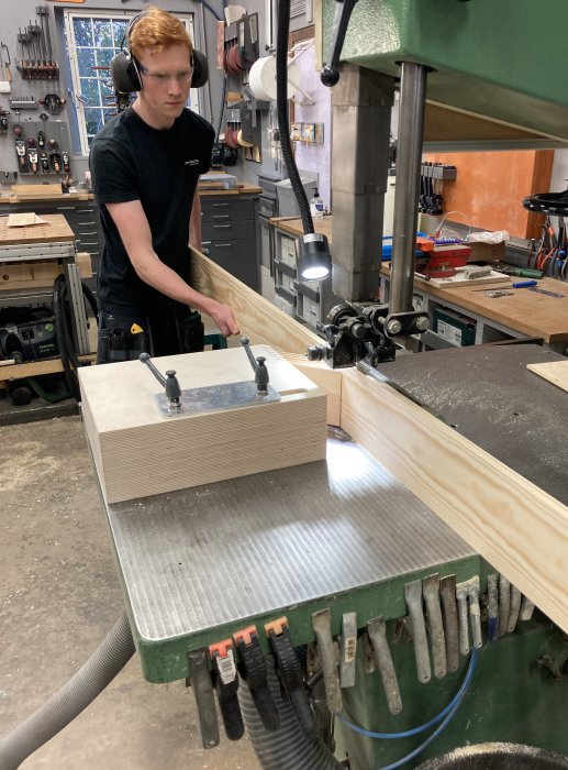 Person använder en featherboard för att såga fanér på bandsåg i verkstad.