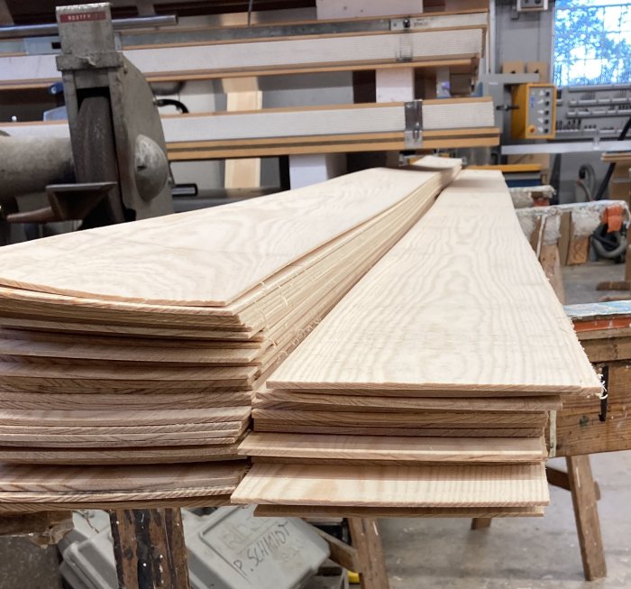 Hög med nysågade fanérplankor på arbetsbänk i verkstad.