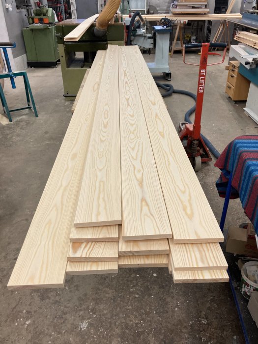 Staplar av nysågade fanérplankor med utmärkt träådring på ett verkstadsgolv.