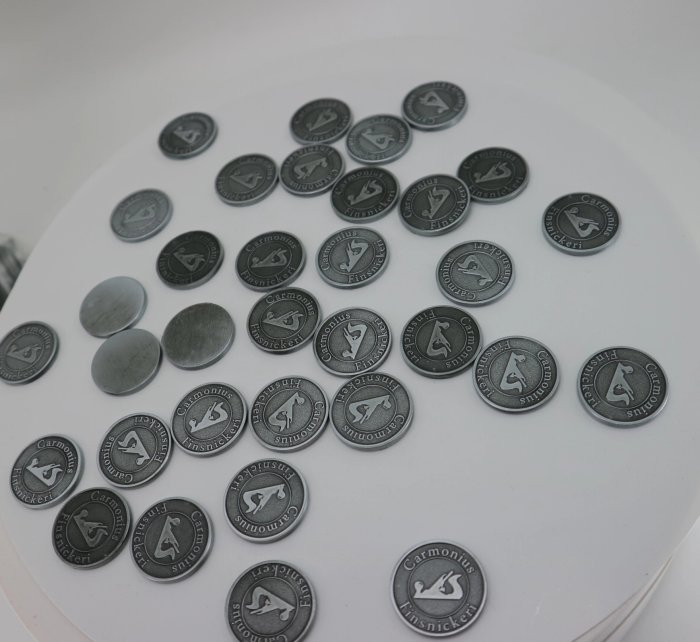 Custom-designed coins scattered on a white surface, used for branding woodworks.