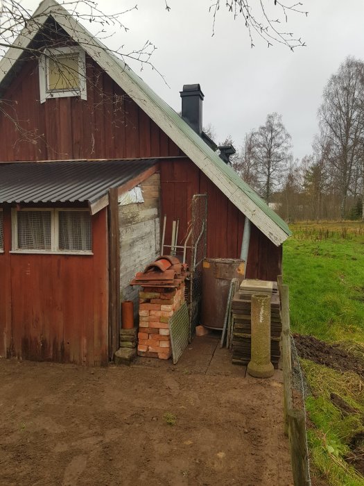 Nyjämnad mark bakom ett rött skjul med trädgårdsplattor och redskap i hörnet.