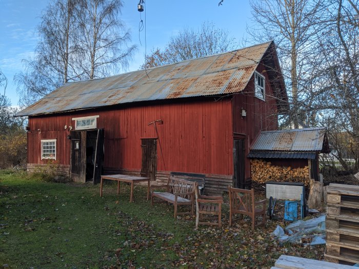 Gammal röd lada med slitet plåttak och trädgårdsmöbler framför.