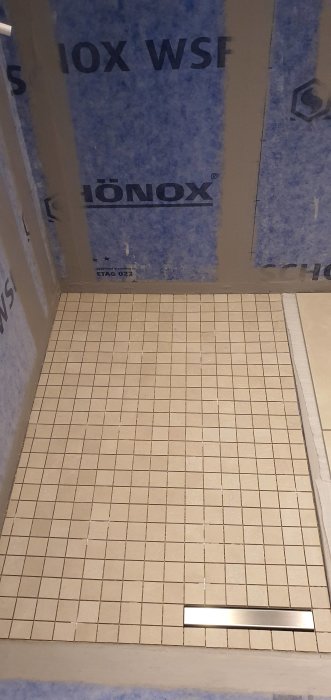 Mosaik i beige Emilceramica Be-Square Sand på duschgolv med noggrann passning kring avloppsbrunnen, mot blått vattentätt membran.