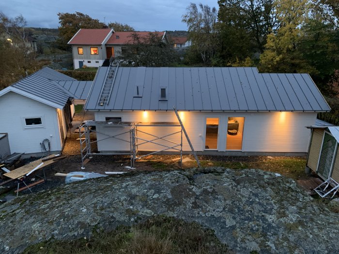 Nyrenoverat hus med grått tak och vita väggar i skymningen, byggställning vid sidan.