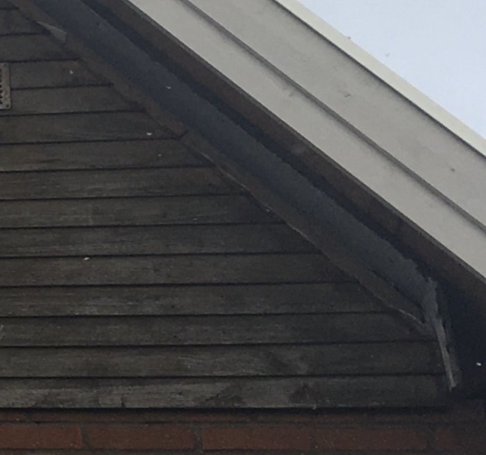 Väderbiten liggande träpanel på husfasad under ett takutsprång.