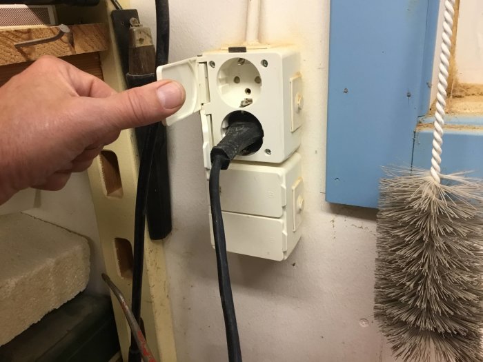 Person öppnar lock på vägguttag med tummen för att sätta i en stickpropp.