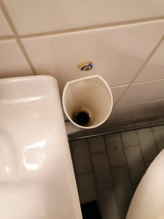 Rörutstick i badrum intill kakelvägg och svart klinkergolv, möjlig plats för tvättmaskin.