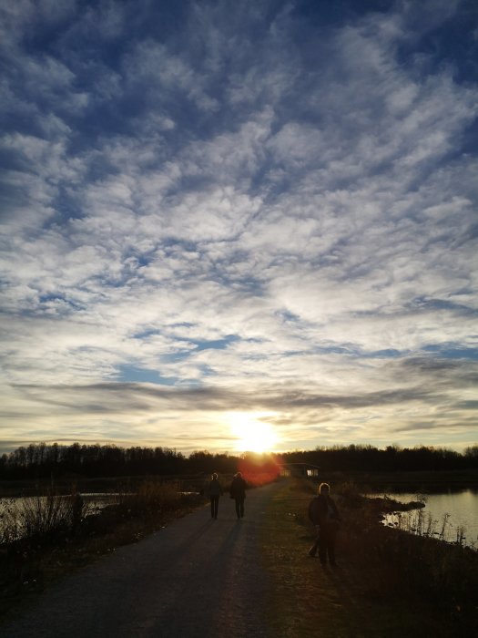 Personer som promenerar längs motionsspåret Rävgången i Örebro vid solnedgång med dramatisk himmel.