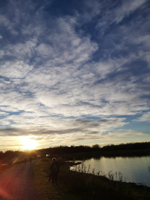 Personer på motionsspår vid sjö i Örebro under solnedgång med molnig himmel.