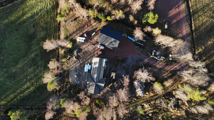 Drönarvy av byggprojekt med halvfärdigt hus och material spridda runtomkring på tomten.