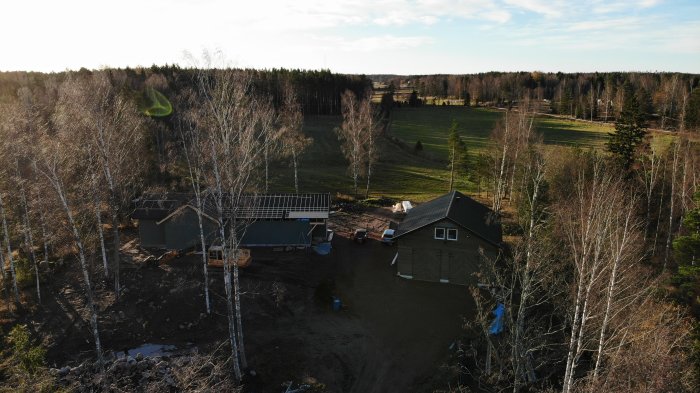 Drönarvy över byggarbetsplats med halvfärdigt hus och omgivande natur.