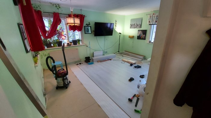Nylagt laminatgolv i stuga med verktyg och allmogelister på golvet, redo för storstädning.