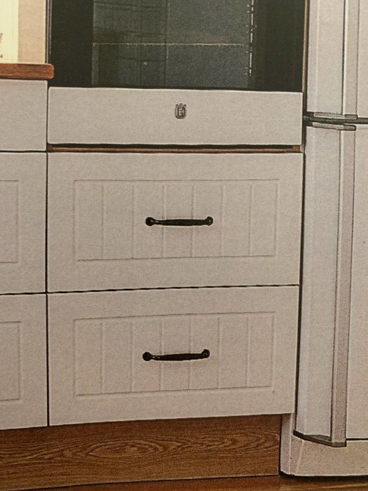 Vit köksinredning med svarta handtag och okänd logotyp på låda.