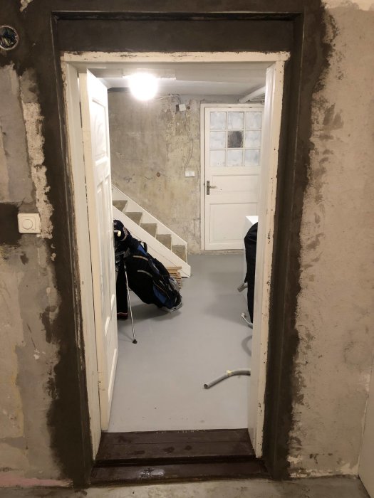 Renoveringsarbete med ojämnt lagt lagningsbruk på väggar i ett halvfärdigt rum med vita dörrar och golfklubbor.