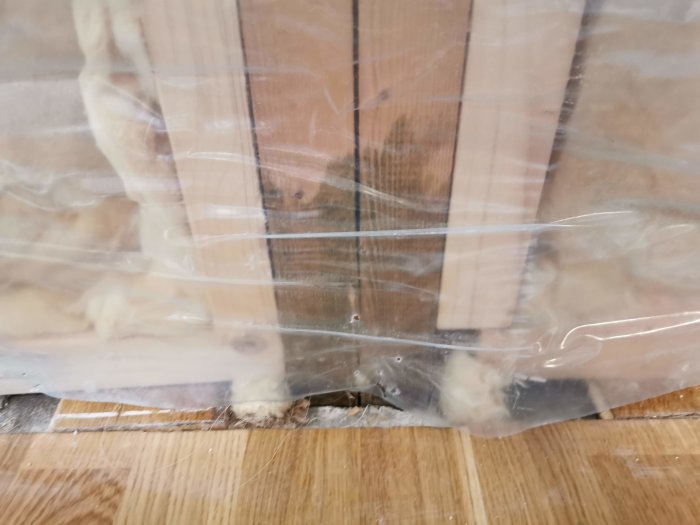 Visuell inspektion av träreglar och impregnerad syll genom plastskydd.