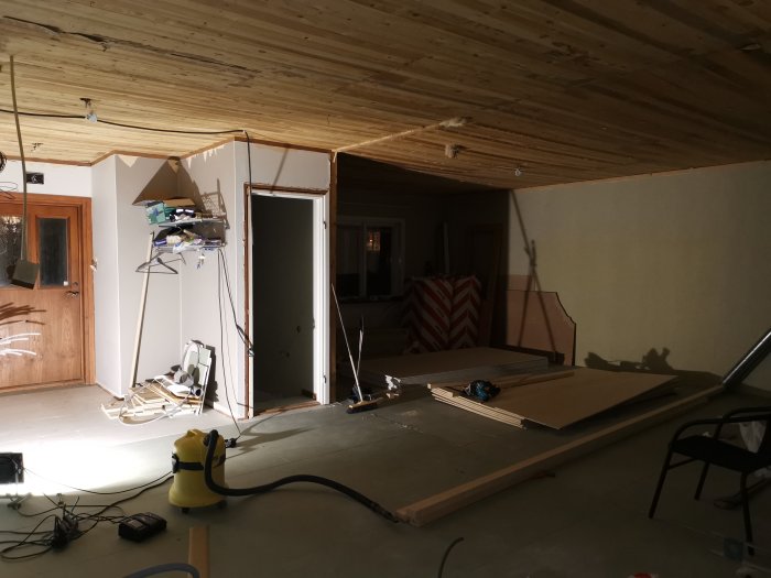 Pågående renovering i en hemmiljö med plywood och gipsplattor förberedda för väggar, och isoleringsmaterial synligt.