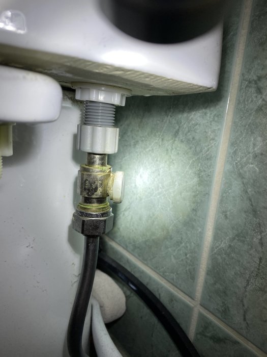 Vattenanslutning till toalettcistern med möjliga rostavlagringar och kopplingar.