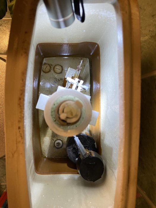 Öppen toalettcistern som visar rödaktig sedimentansamling och delar av spolmekanismen.