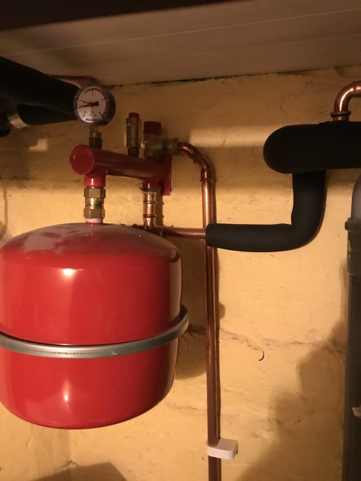 Värmesystem med tryckmätare och rörkopplingar ovanpå en röd expansionskärl.