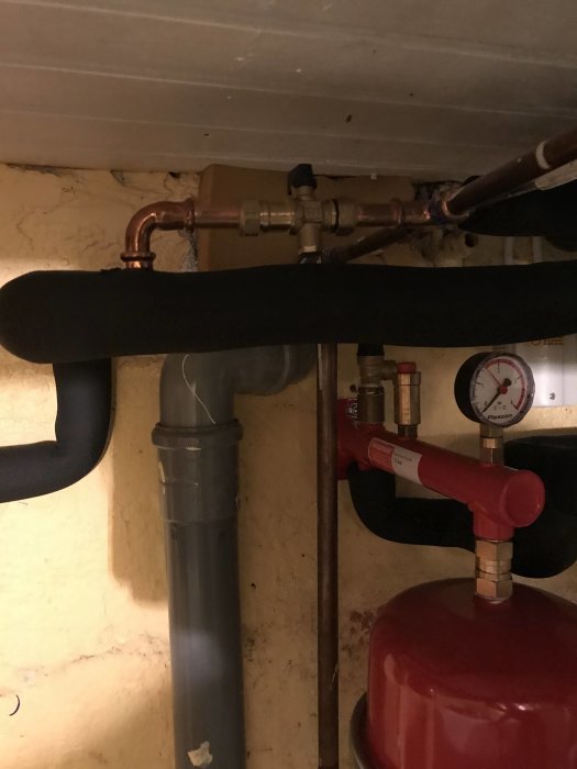VVS-installation med rör, en röd ventil och en tryckmätare under en vit bänkskiva.