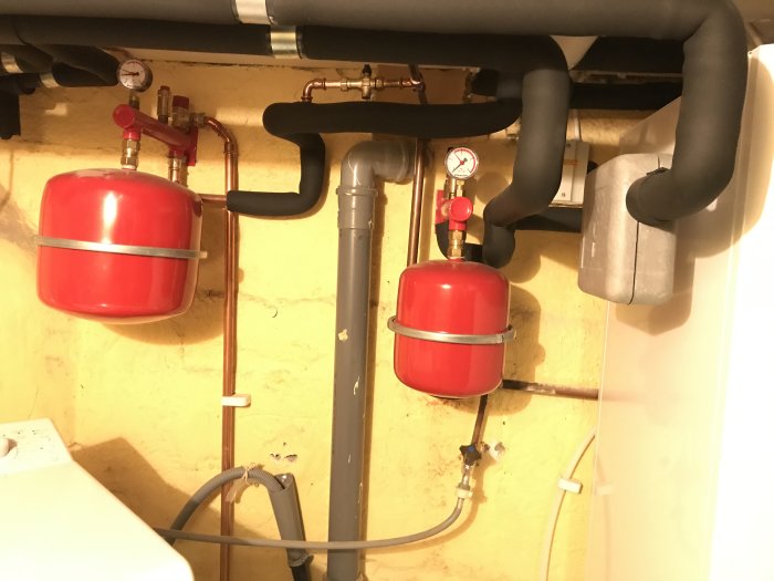 Rörinstallation med två röda expansionskärl, vänster för värme och höger för kyla, och manometer.