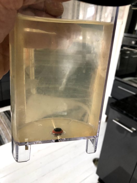 Hand håller transparent behållare med gulaktigt vatten som indikerar föroreningar.