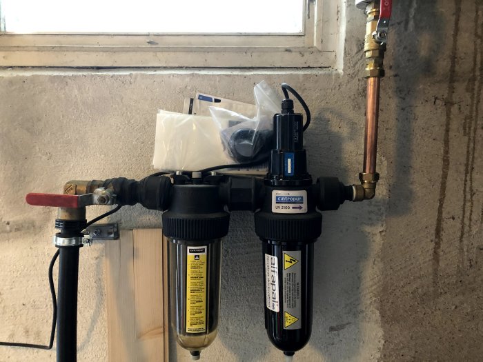 Vattenfiltreringssystem med filter och uv-ljusrenare kopplade till kopparledningar och plastslang.